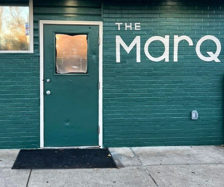 A green brick wall with a green door and a window. Large white letters on the wall spell 