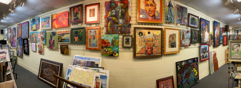 A panoramic view of an art gallery with colorful paintings and portraits displayed on cream-colored walls, framed artwork filling the space from floor to ceiling, creating a vibrant and eclectic atmosphere.