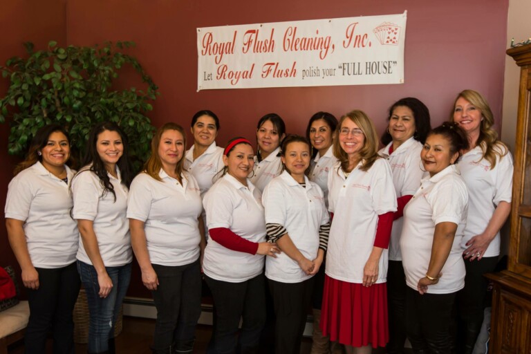 A group of twelve smiling women wearing matching white polo shirts stands together indoors in front of a 