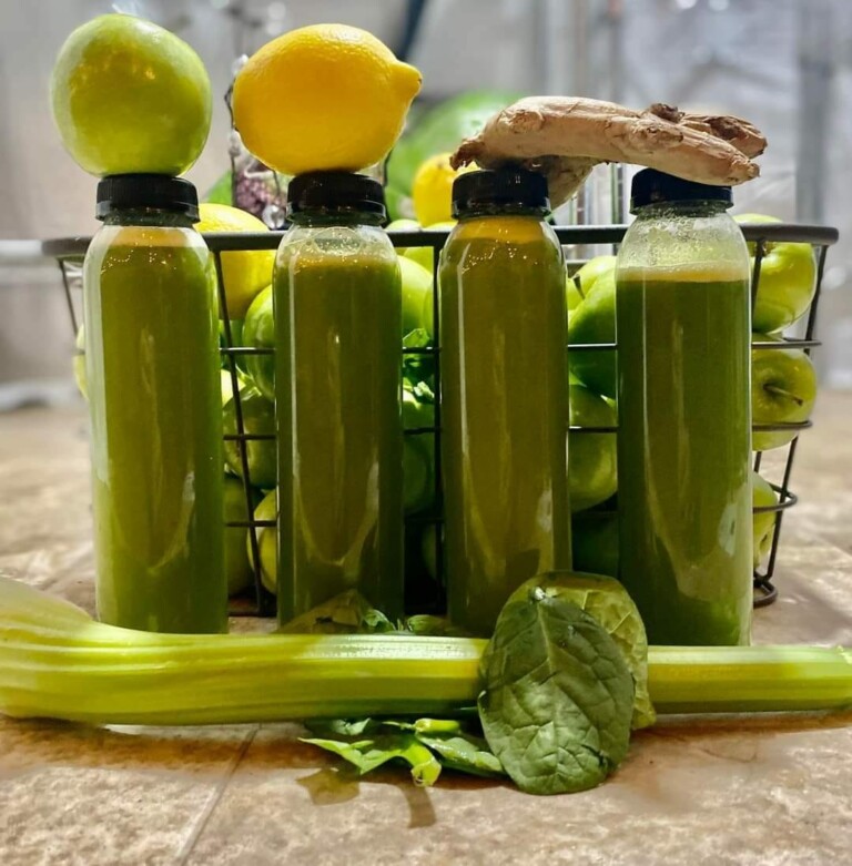 Four bottles of green smoothie juice. A lemon, lime, celery, and ginger shown.