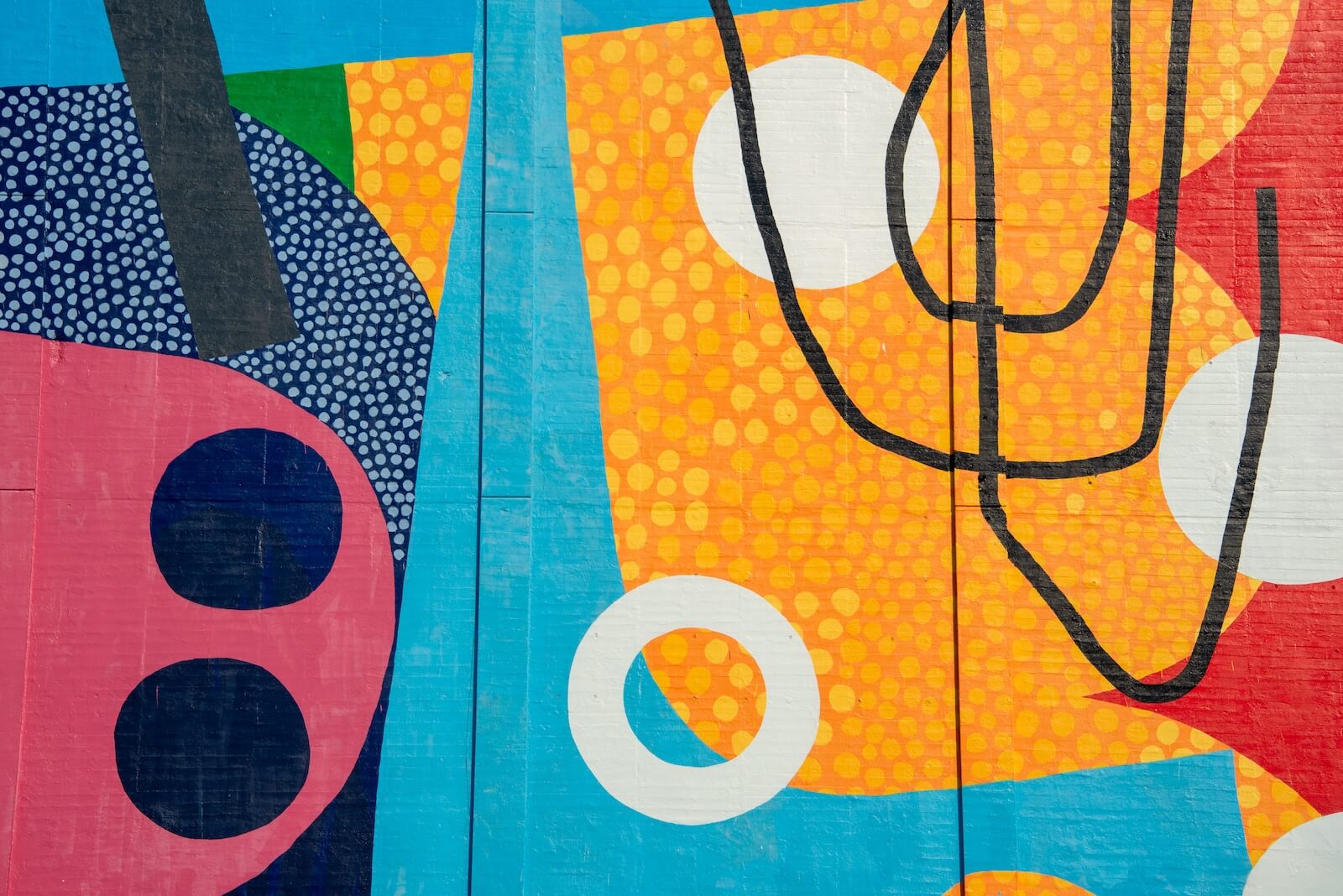 Colorful abstract mural featuring bold shapes, dots, and lines in blue, yellow, red, black, and white, with overlapping patterns and contrasting textures.